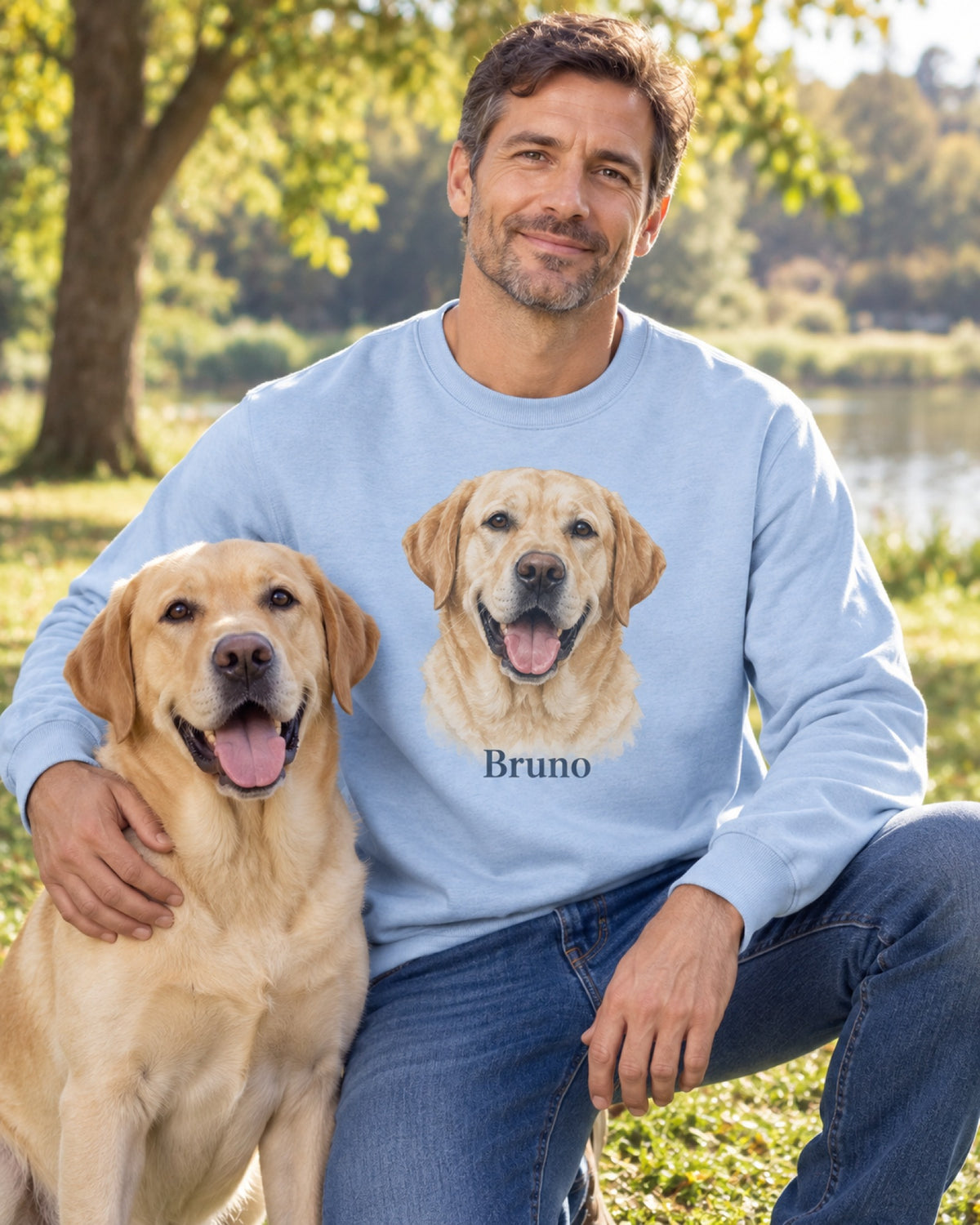 Hellblaues Sweatshirt mit Labrador im Aquarell-Stil und Namen Bruno, der Mann kniet mit seinem Labrador im Park am See