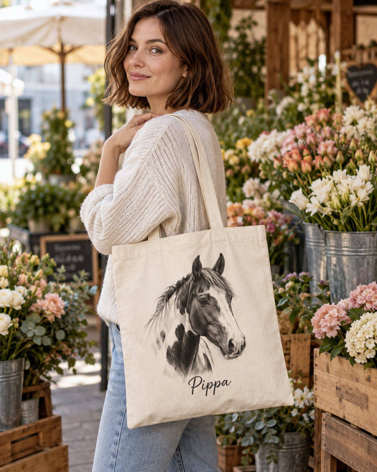 Frau mit naturfarbener Stofftasche mit Pferdeportrait als Zeichnung und Namen Pippa am Blumenstand