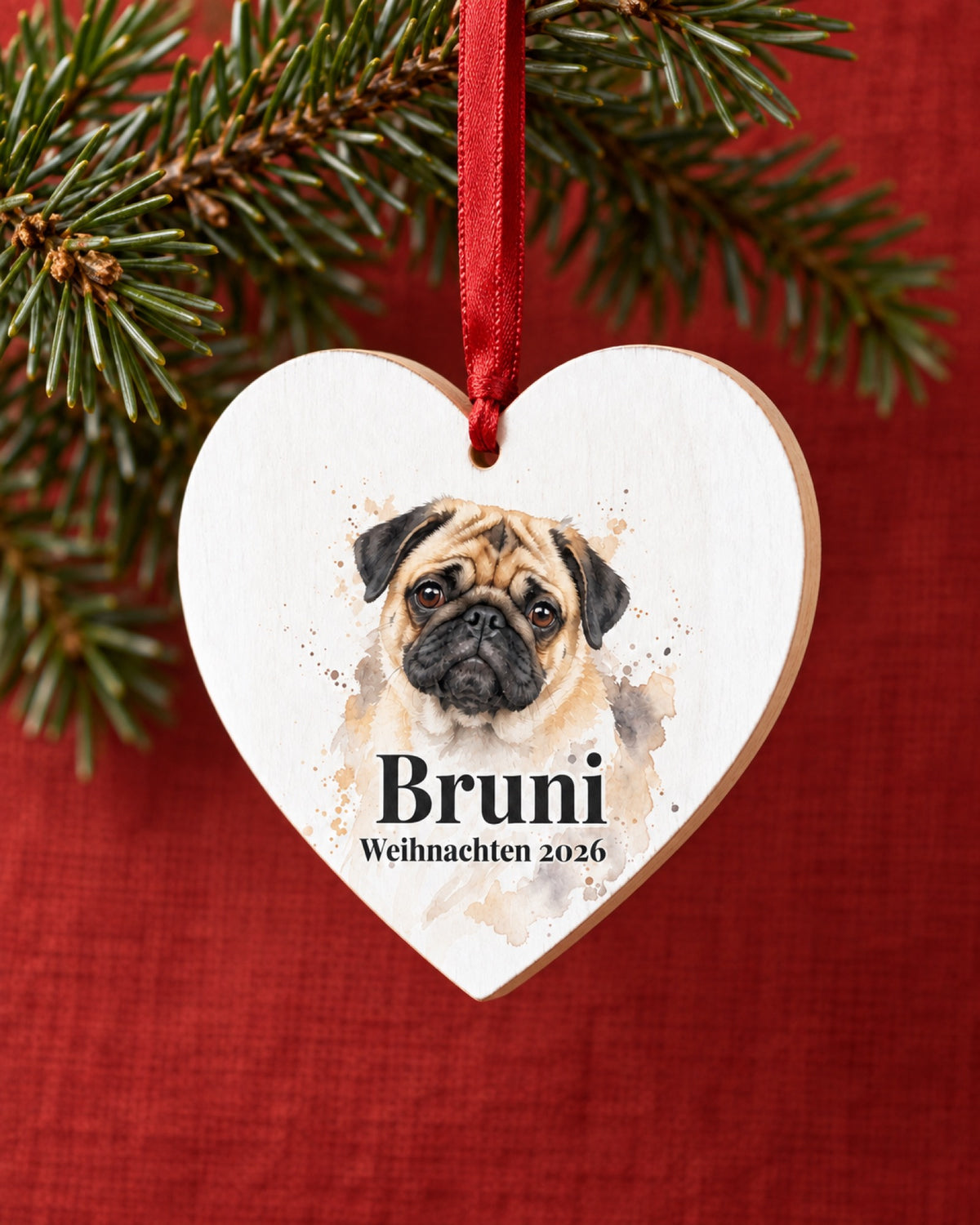 Baumschmuck aus Holz als Herz mit Mops Bruni an einem kleinen grünen Zweig vor einer roten Leinenwand