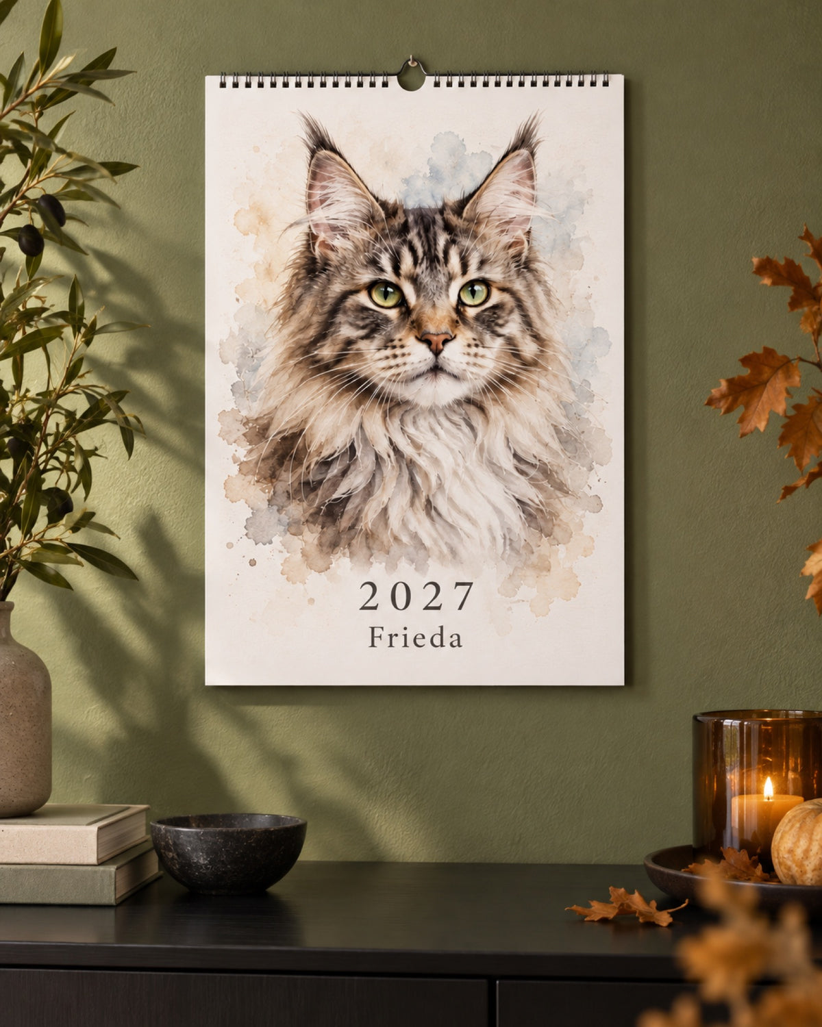 Maine Coon Frieda auf dem Titelblatt des Haustier Wandkalenders 2027 an einer olivgrünen Wand über einem schwarzen Sideboard im Herbst