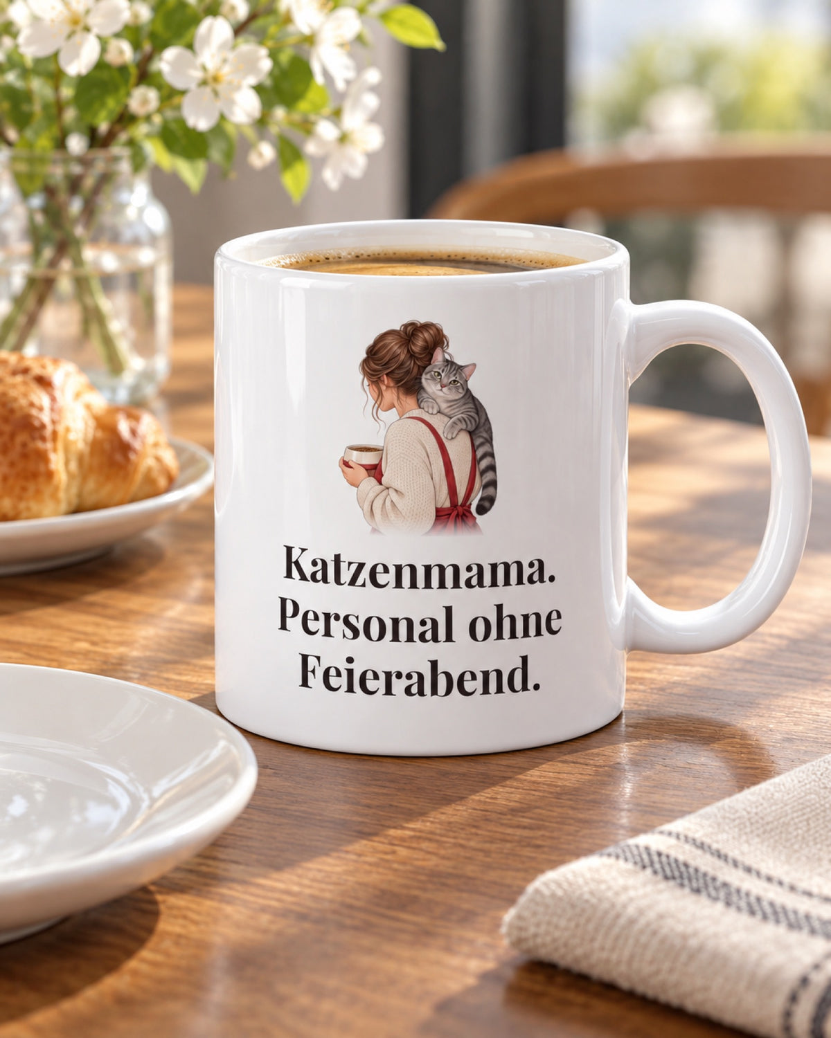 Weiße Keramiktasse Katzentasse mit Spruch: Katzenmama. Personal ohne Feierabend. auf einem Cafétisch im Frühling