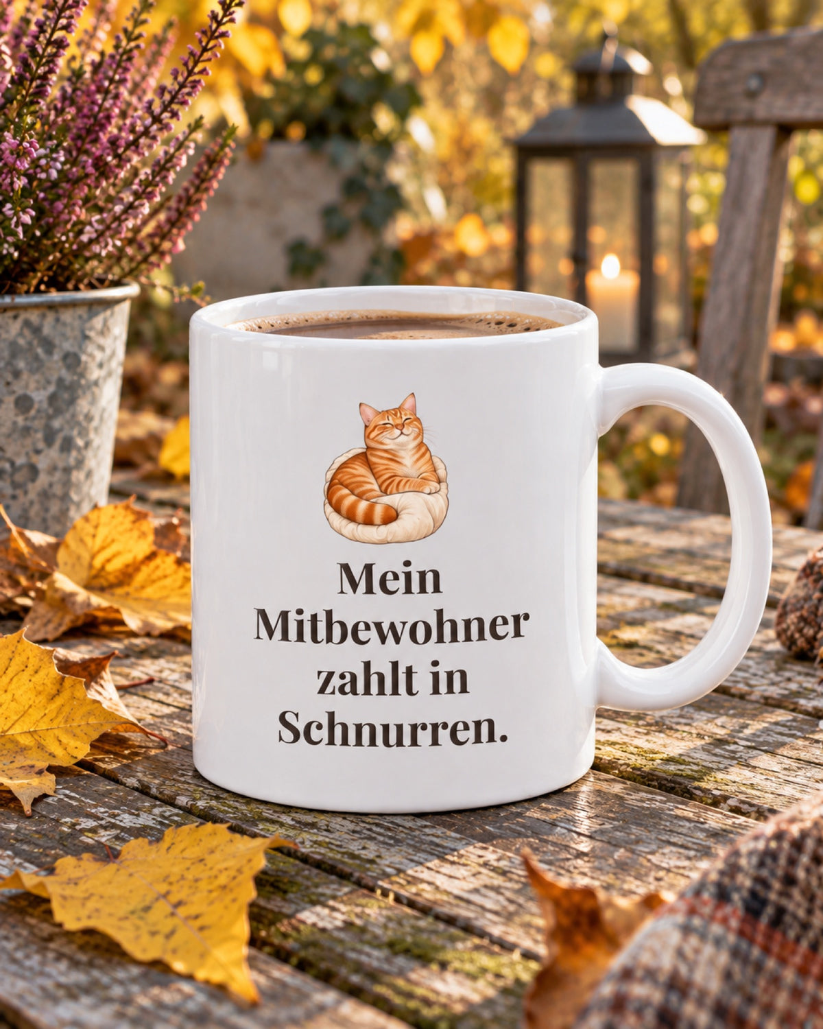 Weiße Keramiktasse Katzentasse mit Spruch: Mein Mitbewohner zahlt in Schnurren. auf einem Gartentisch im Herbst