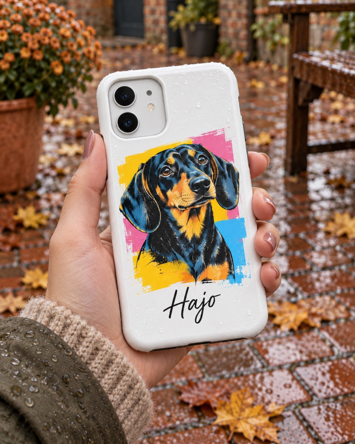 iPhone 11 Hülle mit Dackel im Pop-Art-Stil und Namen Hajo auf einem regennassen Ziegelhof in der Hand einer Frau im Herbst