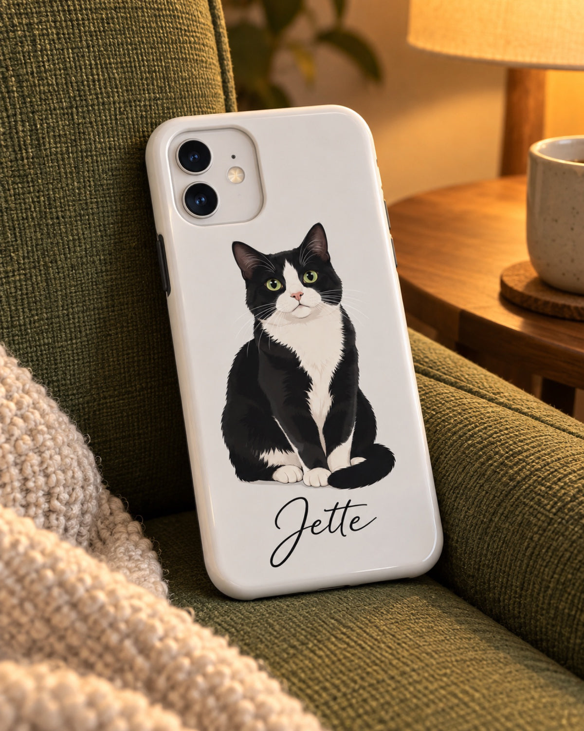 iPhone 11 Hülle mit schwarz-weißer Katze im Cartoon-Stil und Namen Jette auf einem grünen Lesesessel bei warmem Abendlicht